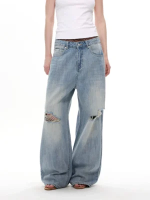Front partial view of light blue sun-faded arc balloon wide-leg distressed Y2K jeans with ripped knees and relaxed streetwear fit