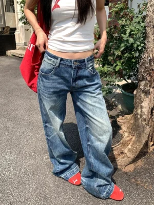 Woman wearing sun-faded low-rise wide-leg blue jeans in a relaxed streetwear outfit on a residential garden street
