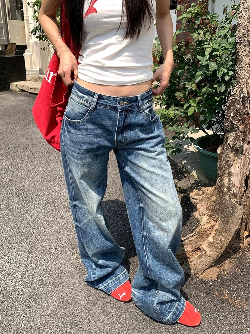 Woman wearing sun-faded low-rise wide-leg blue jeans in a relaxed streetwear outfit on a residential garden street