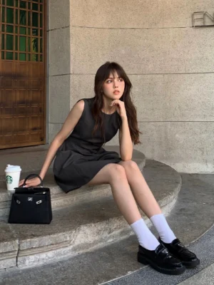 Dark gray sleeveless tailored A-line mini dress styled with white socks and leather loafers on outdoor concrete steps