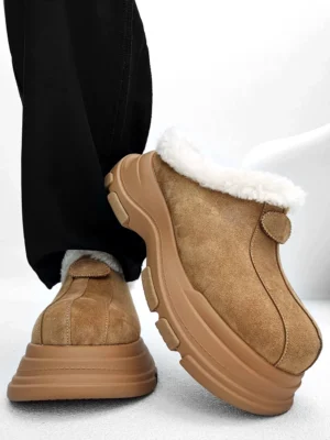 Tan brown fleece-lined chunky platform clogs shown from a rear low angle with fluffy faux-fur collar, rugged anti-slip rubber outsole, and black loose trousers