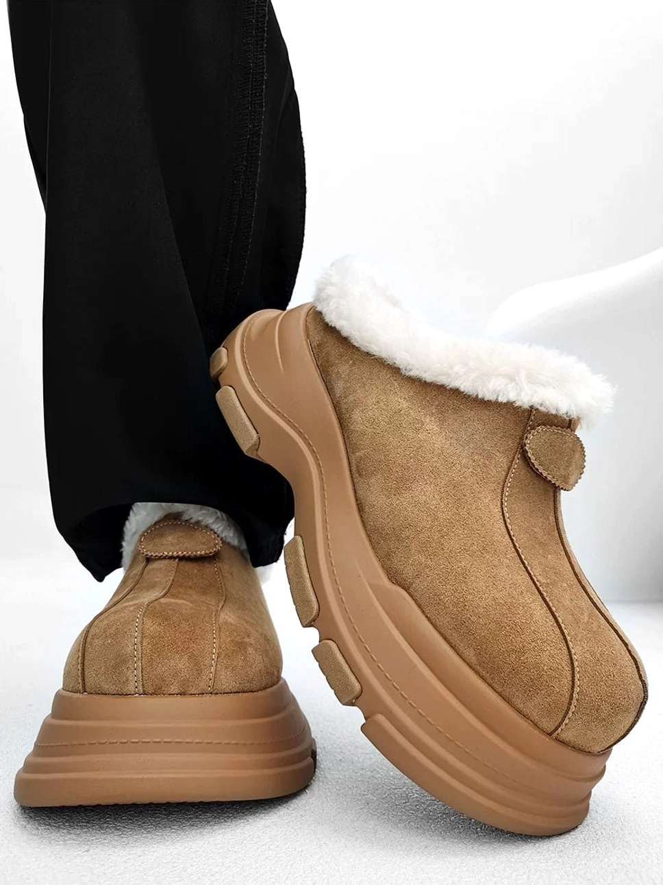 Tan brown fleece-lined chunky platform clogs shown from a rear low angle with fluffy faux-fur collar, rugged anti-slip rubber outsole, and black loose trousers