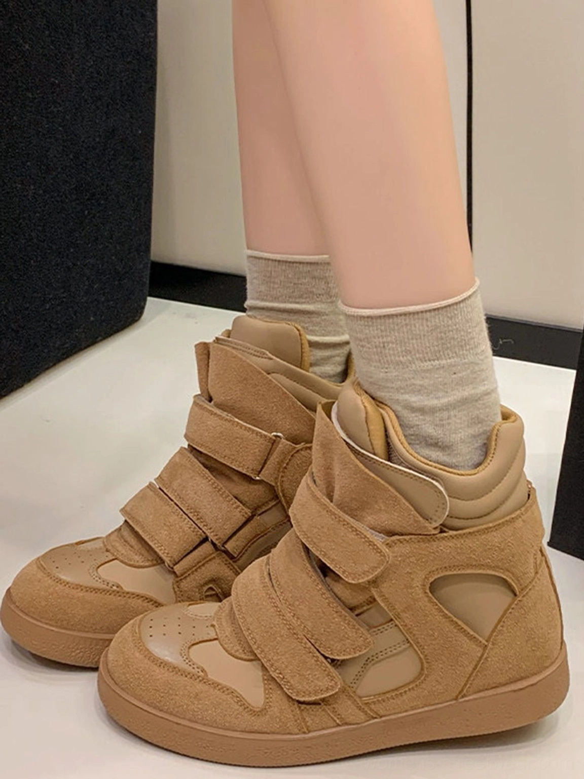 Women's tan brown hidden-wedge high-top sneakers worn with beige crew socks, featuring a monochrome suede upper and matching gum sole
