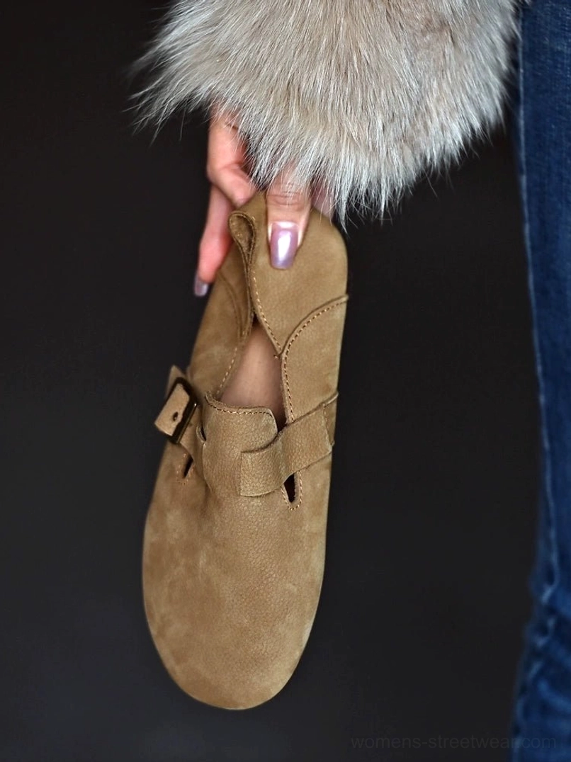 Top-down close-up of a tan buckle loafer held above blue denim, showing the textured leather upper and collapsible heel