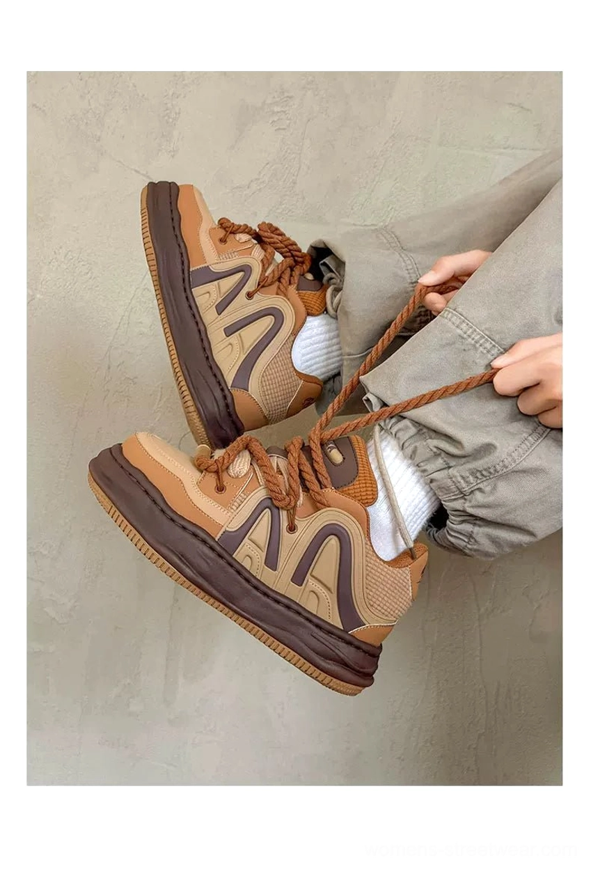 Tan and dark brown chunky platform sneakers with oversized rope laces and sculpted side details, styled with relaxed gray trousers