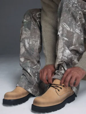 Male model wearing tan full-grain leather lug sole derby shoes with camouflage pants in a streetwear studio outfit