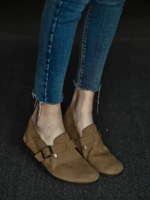 Tan leather buckle loafers worn with frayed skinny jeans in a low full-body streetwear view, showing the rounded toe and textured upper