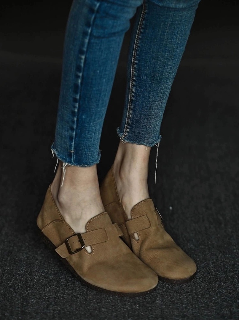 Tan leather buckle loafers worn with frayed skinny jeans in a low full-body streetwear view, showing the rounded toe and textured upper