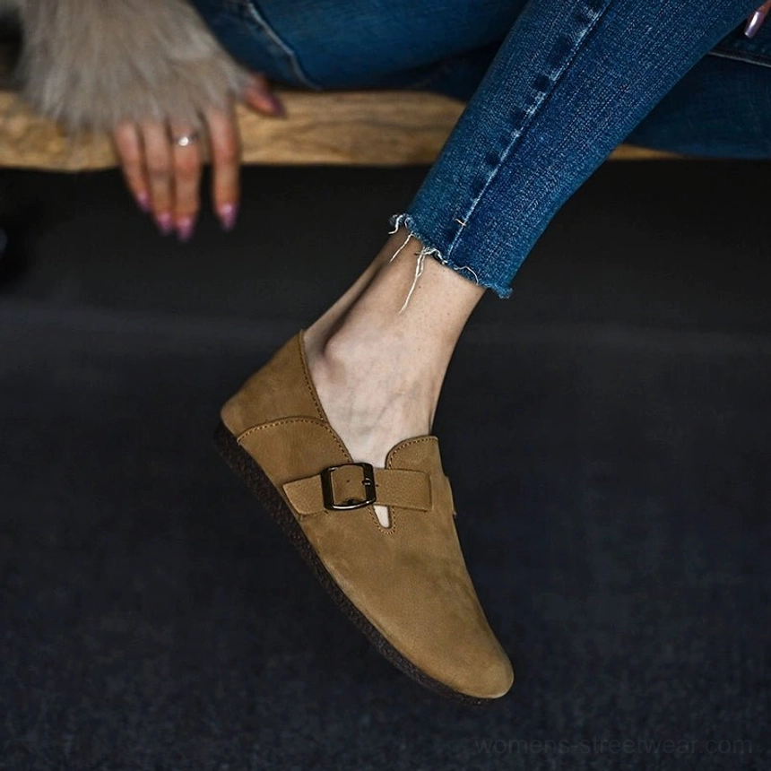 Low angled view of a tan leather slip-on loafer with clean textured finish, functional side buckle, and flat sole