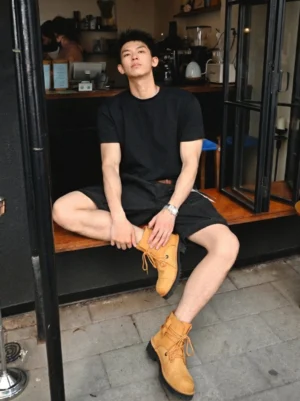 Tan leather utility ankle boots worn with a casual black streetwear outfit in an outdoor cafe setting