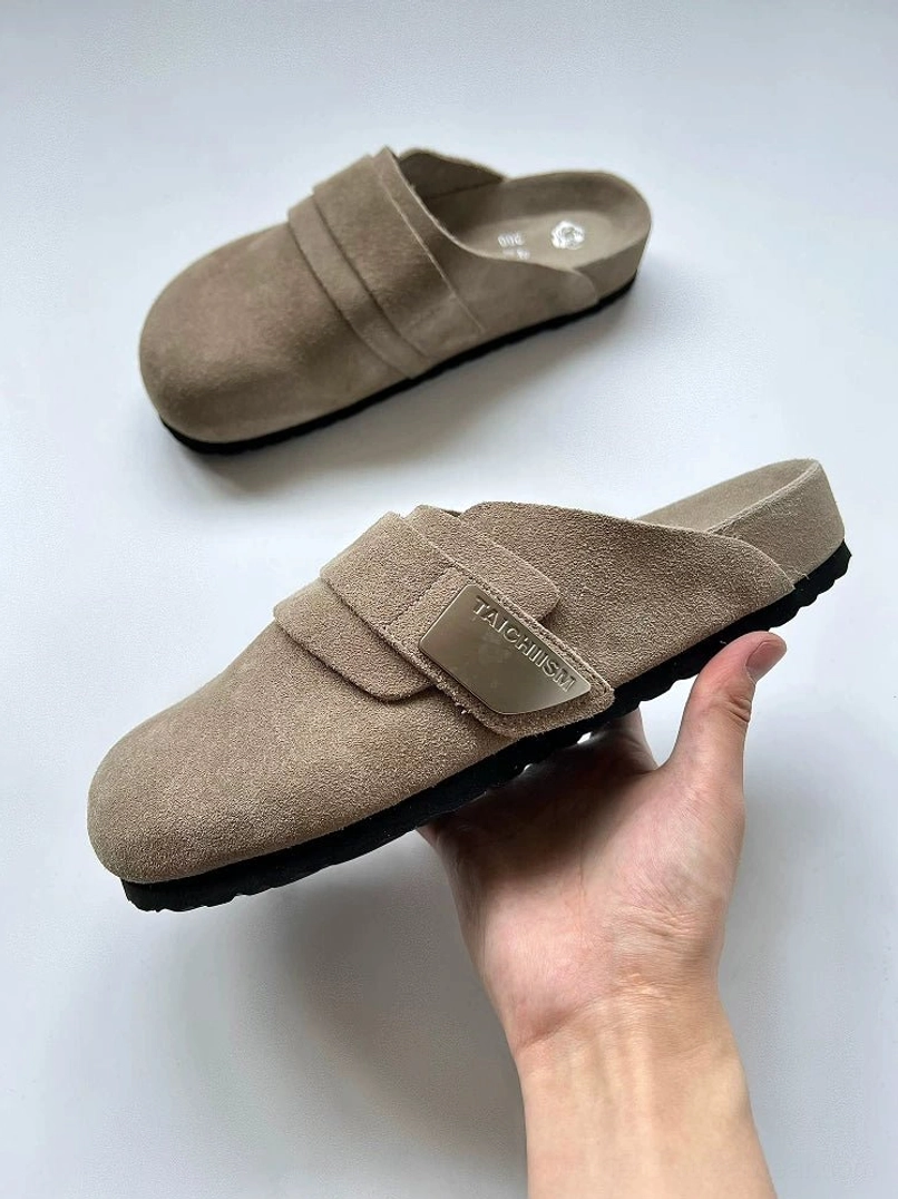 Tan suede leather mule sandals held in hand showing textured upper metal buckle and insole size marking