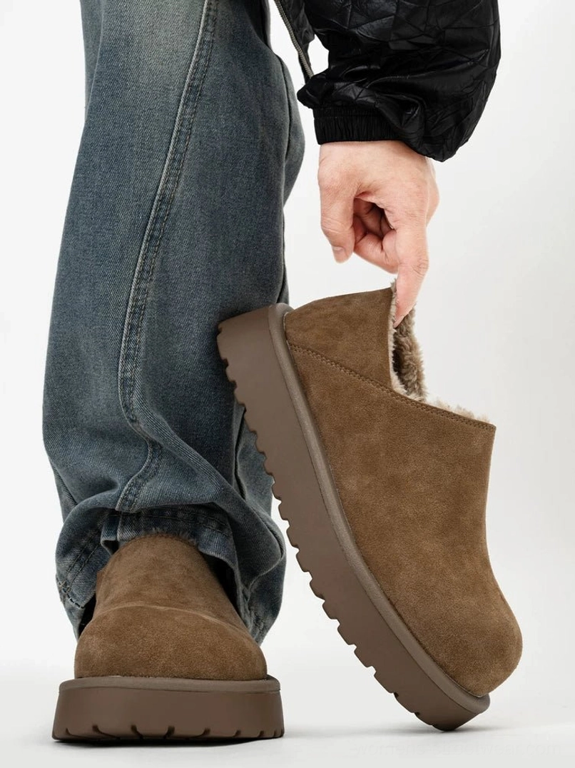 Tan suede shearling-lined platform slip-on clogs worn with blue jeans and black streetwear outerwear, showing the chunky rubber sole and cozy faux fur lining