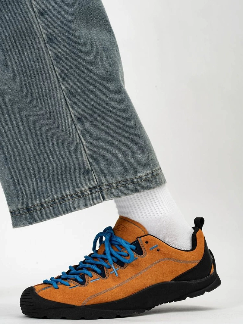 Tan suede streetwear trail sneakers with blue laces, black rugged sole and white crew socks shown in a close on-foot side view