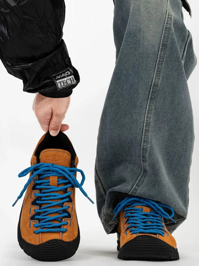 Tan suede trail sneakers with bright blue hiking laces, black rubber toe bumper and rugged outsole shown from front and rear on foot with baggy denim
