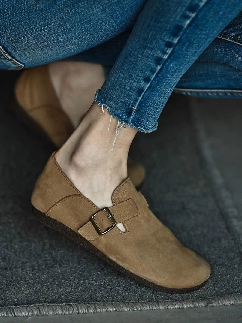 Side angle of a tan textured leather loafer worn with frayed jeans, highlighting the low cork-style sole and buckle strap