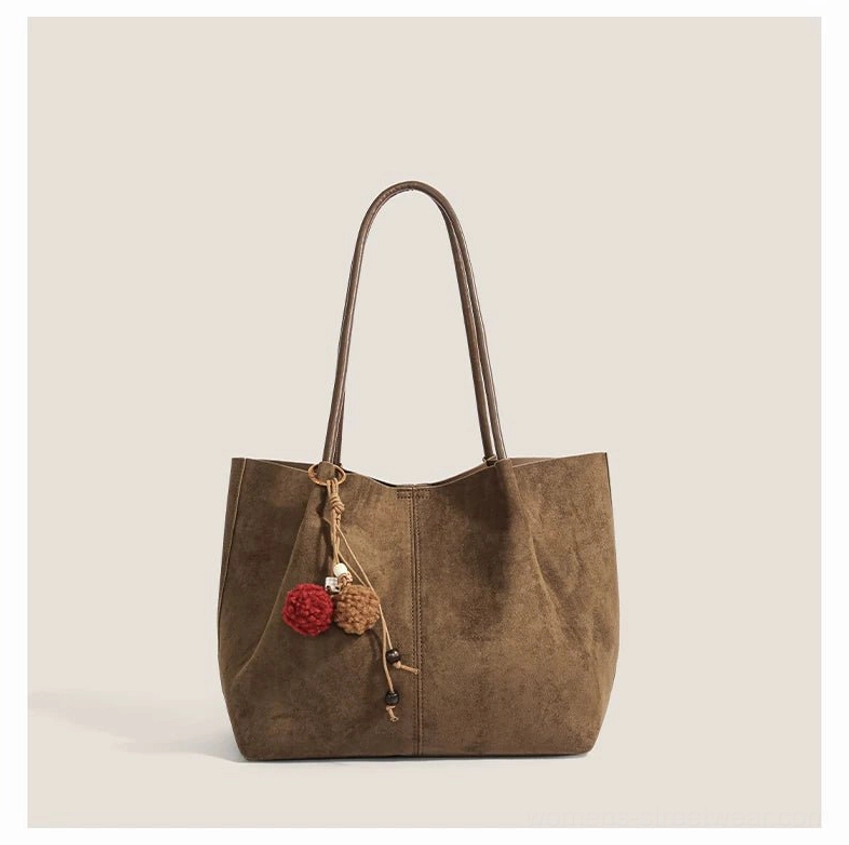 Medium taupe brown faux suede shoulder tote with vertical seam details and decorative pom pom charm for Acubi fashion styling