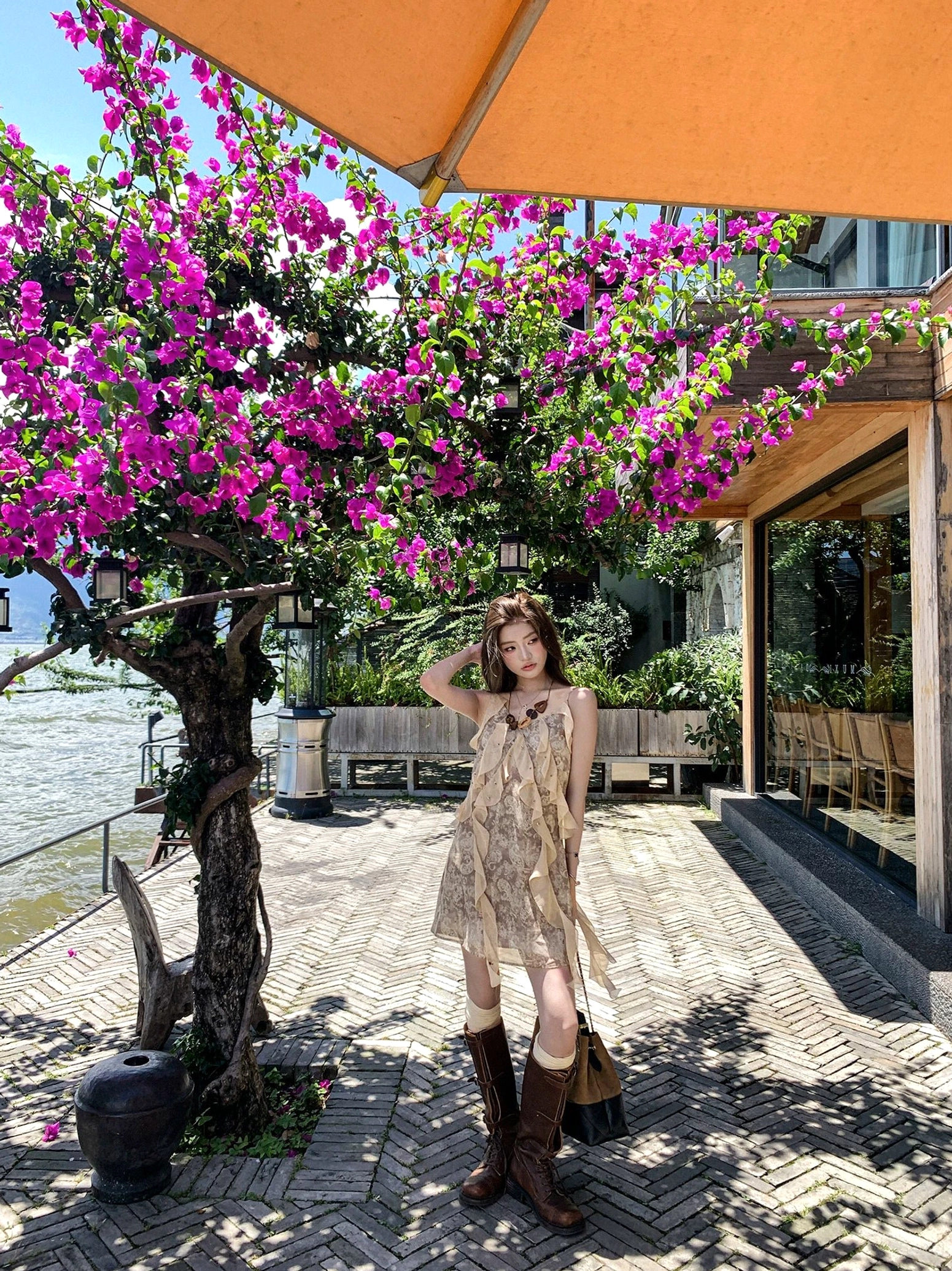 Full body view of taupe floral ruffle slip mini dress styled with brown knee-high boots and a two-tone crossbody bag