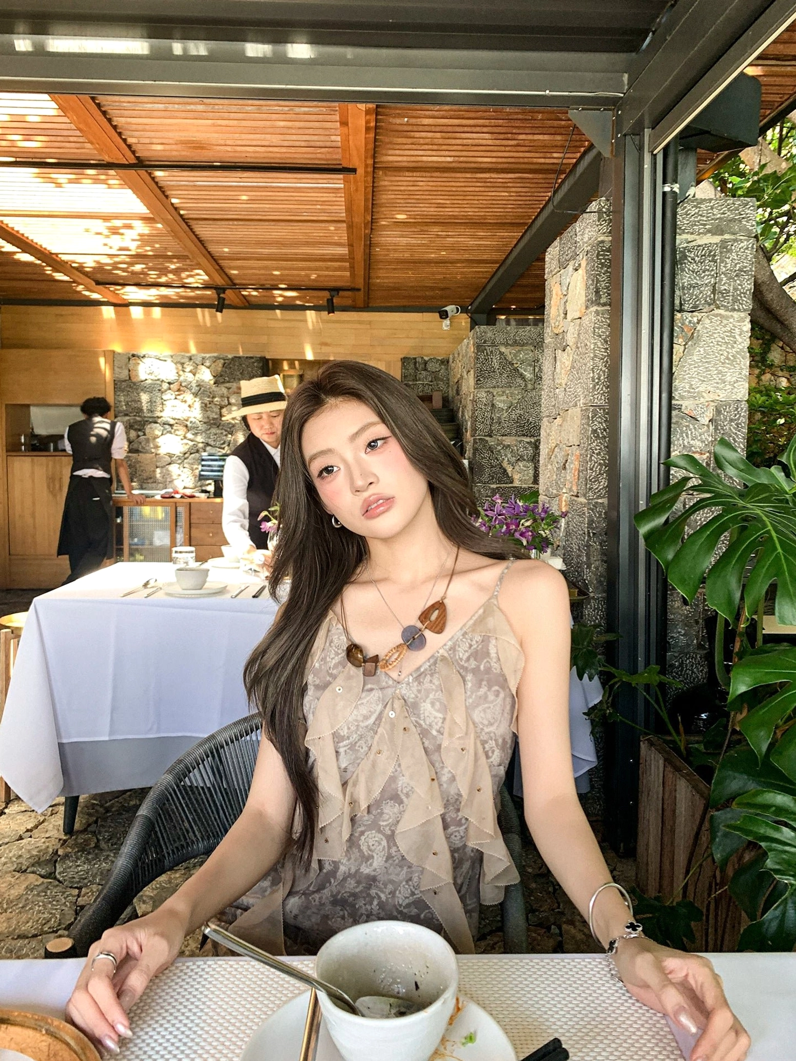 Taupe floral printed ruffle slip mini dress with V neckline and slim spaghetti straps worn at an outdoor restaurant table
