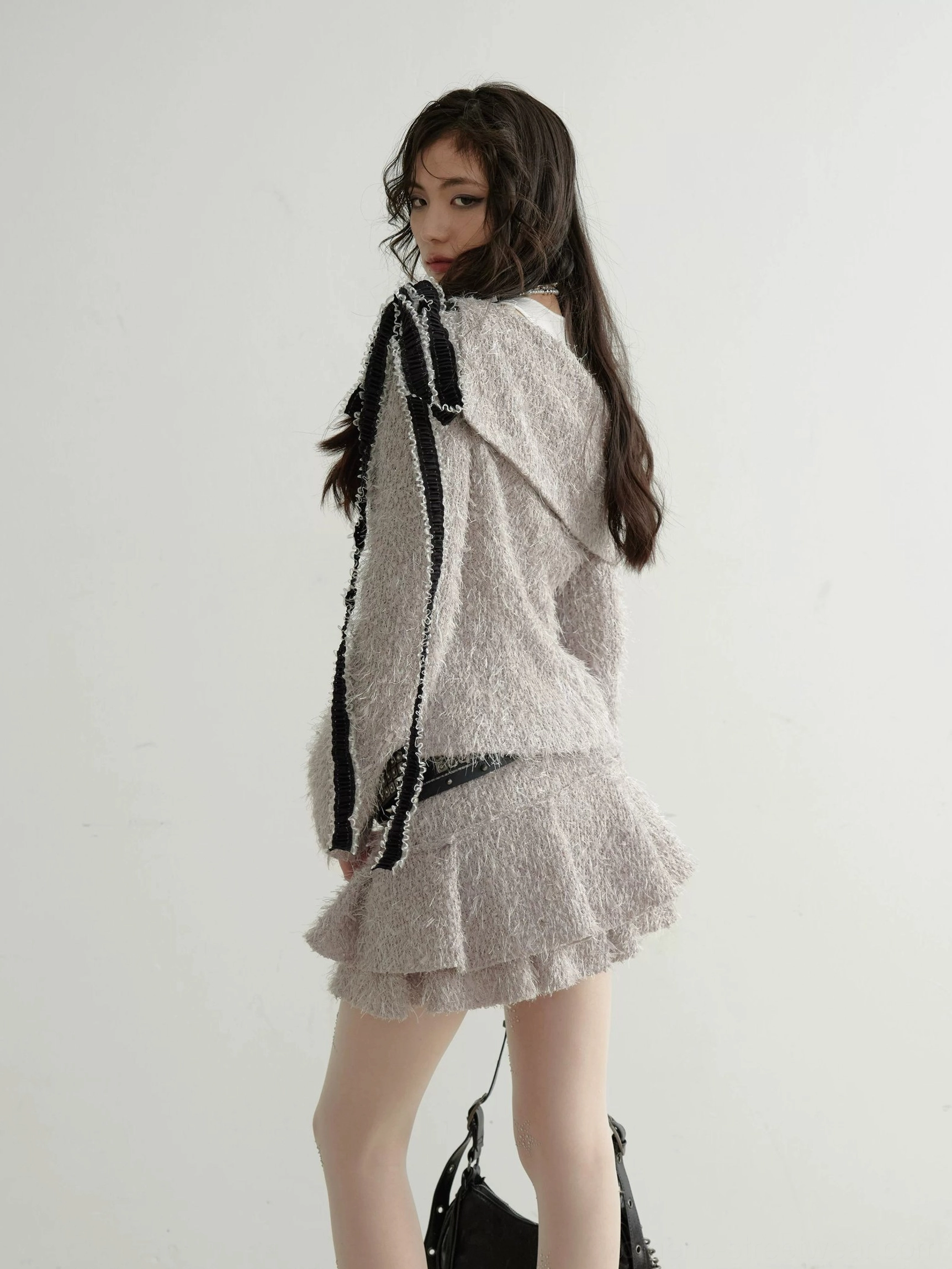 Side back view of taupe fuzzy knit off-shoulder top and ruffle mini skirt with black contrast trim