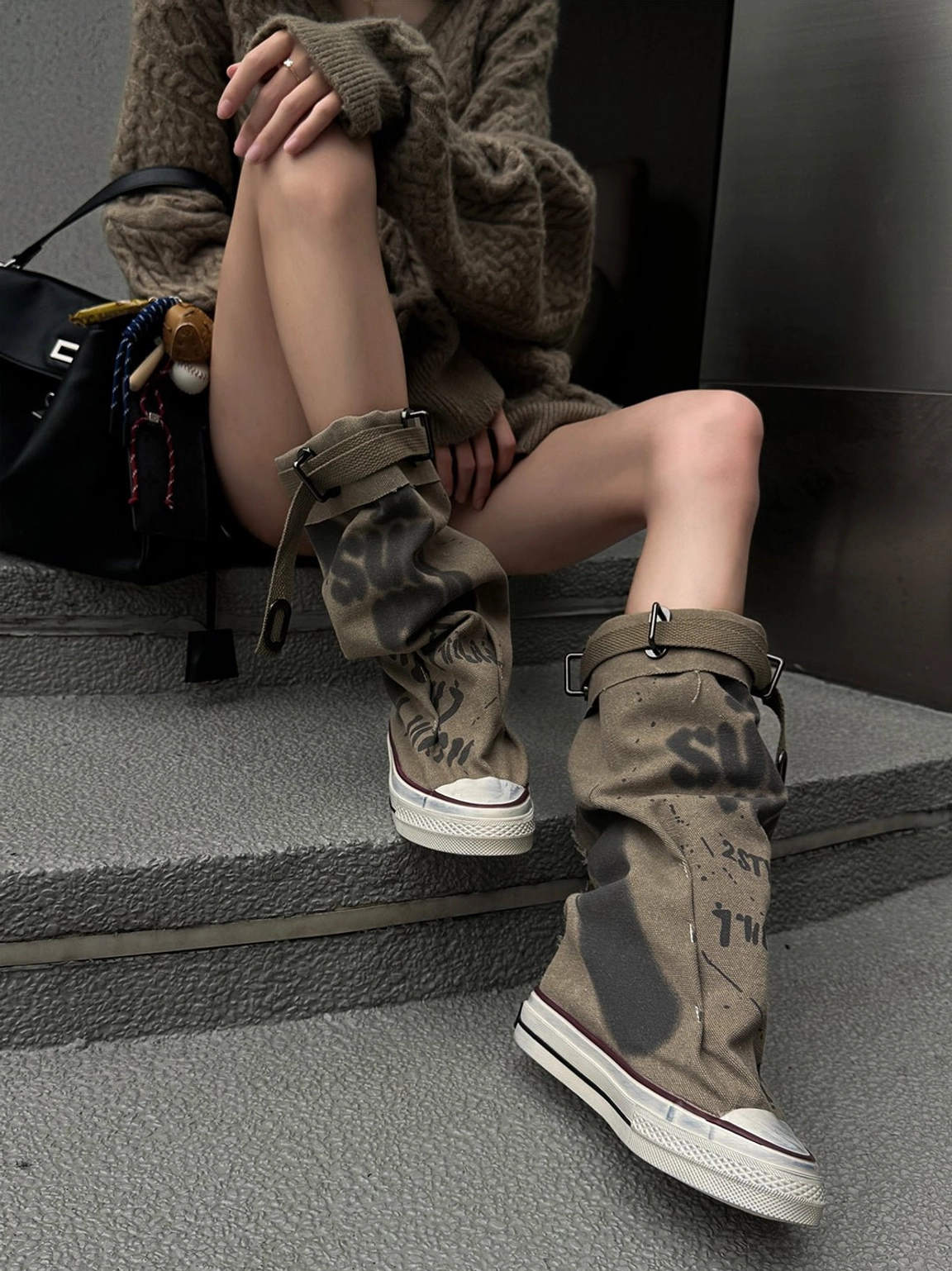 Taupe graffiti canvas lace-up platform tall boots with folded slouchy cuffs and adjustable buckle straps styled on concrete stairs
