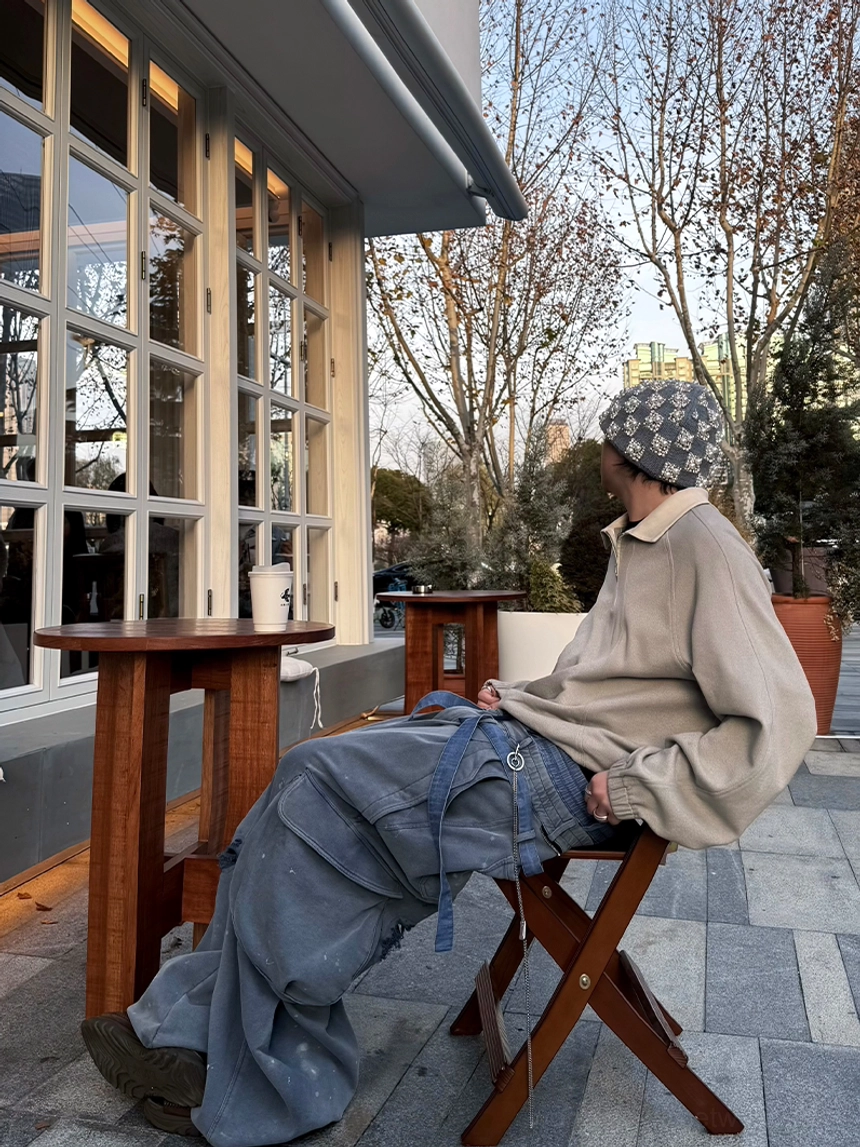 Taupe gray half-zip raglan polo pullover with light contrast collar worn in an outdoor cafe streetwear setting