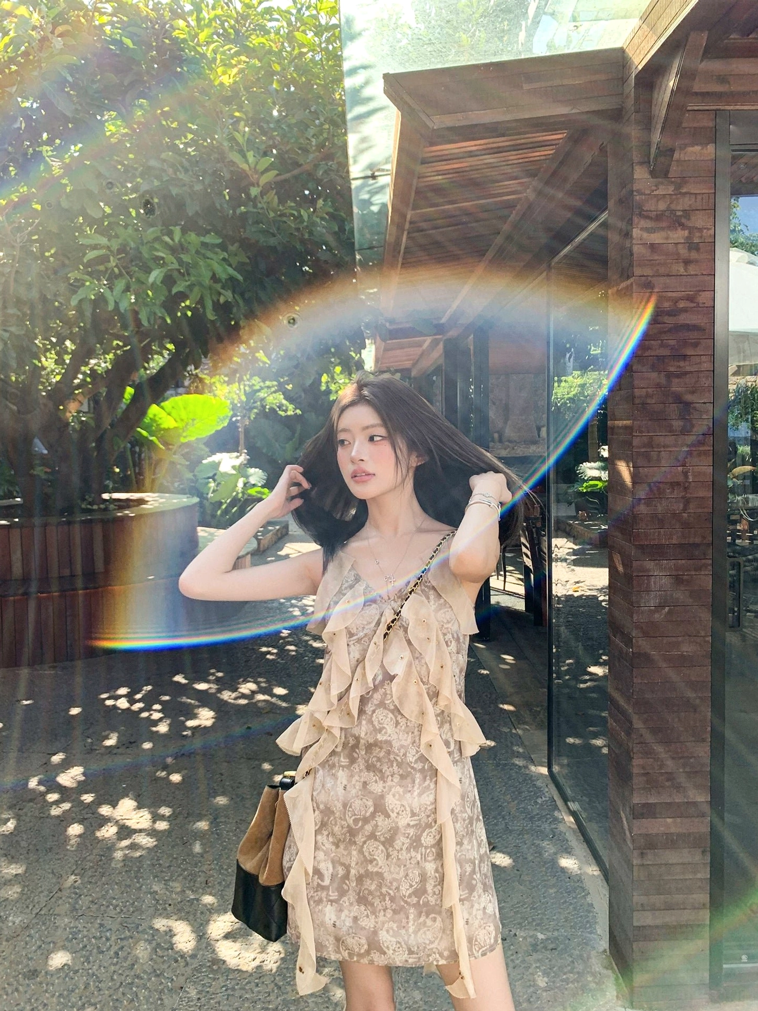 Taupe printed slip mini dress with cascading front ruffles photographed in a sunlit wooden courtyard
