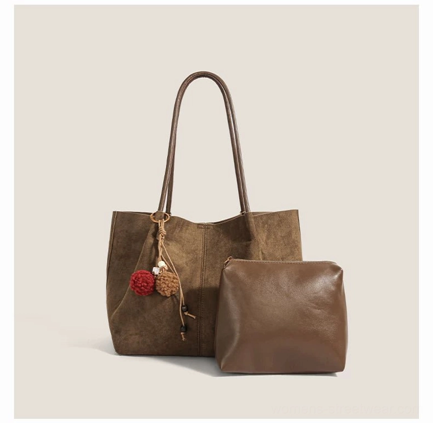 Taupe brown suede tote bag with pom charm shown from a front three quarter angle in minimalist Korean streetwear accessory styling