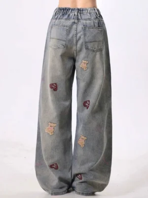 Rear view of teddy bear embroidered wide-leg jeans showing elasticated back waistband, two patch pockets, distressed denim details, and relaxed streetwear fit
