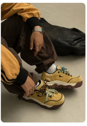 Top view of tan chunky trail sneakers with camouflage patterned laces and thick rugged outsole in a casual indoor setting