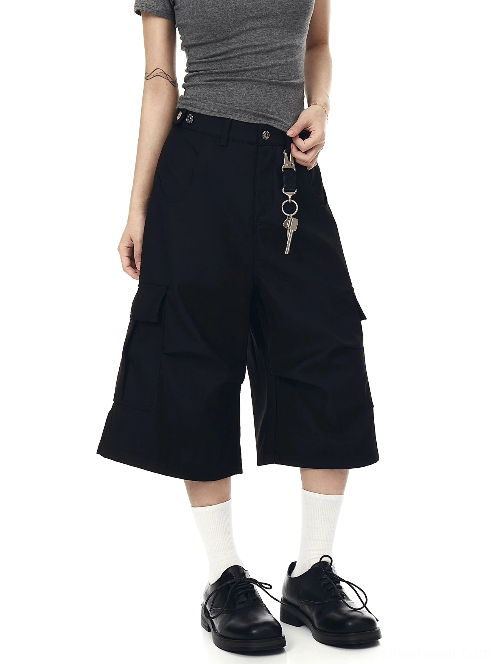 Three-quarter view of all-black oversized cargo culotte shorts with wide cropped legs, side flap pockets, and keychain ornament