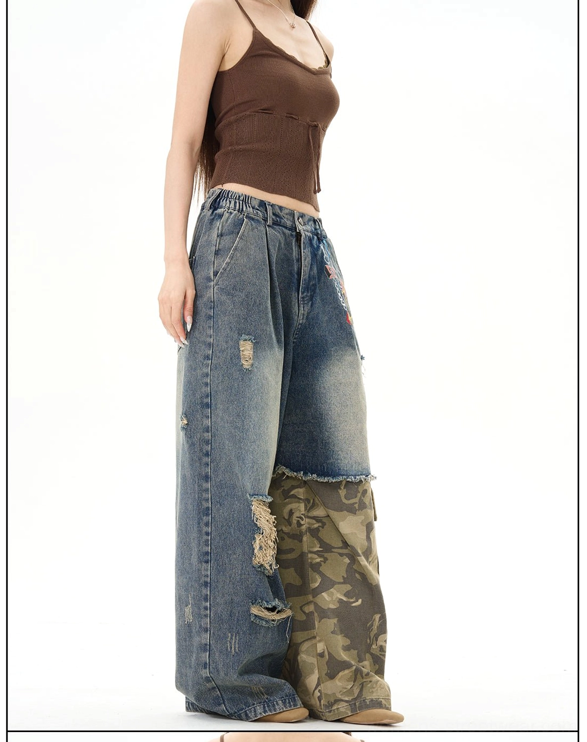 Three-quarter front view of distressed patchwork wide-leg jeans, highlighting washed blue denim, camo lower-leg patchwork, loose silhouette, and frayed ripped details