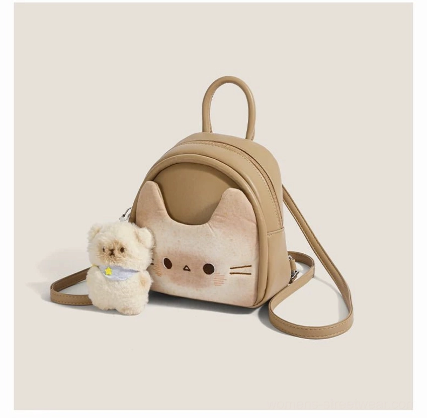 Front view of a cute toast beige cat mini backpack with embroidered eyes and whiskers, full zippered compartment, and fluffy puppy ornament with blue scarf