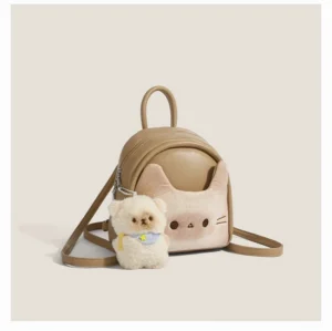 Front left three quarter view of a toast beige kawaii cat mini backpack with embroidered cat face, soft faux leather body, adjustable shoulder straps, top handle, and fluffy puppy charm