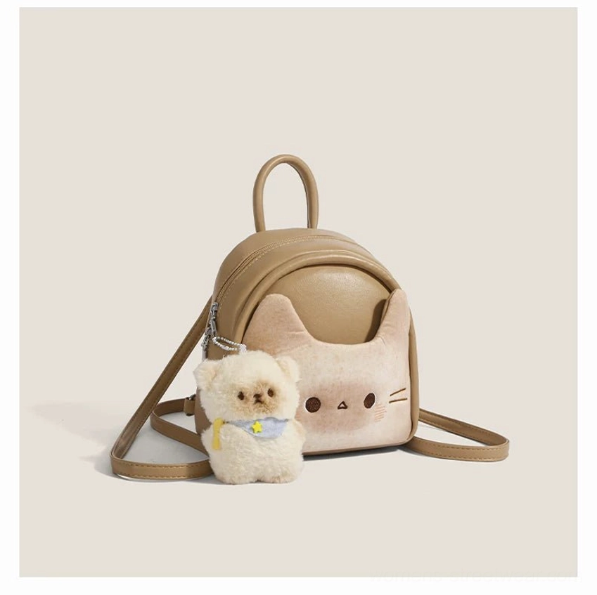 Front left three quarter view of a toast beige kawaii cat mini backpack with embroidered cat face, soft faux leather body, adjustable shoulder straps, top handle, and fluffy puppy charm