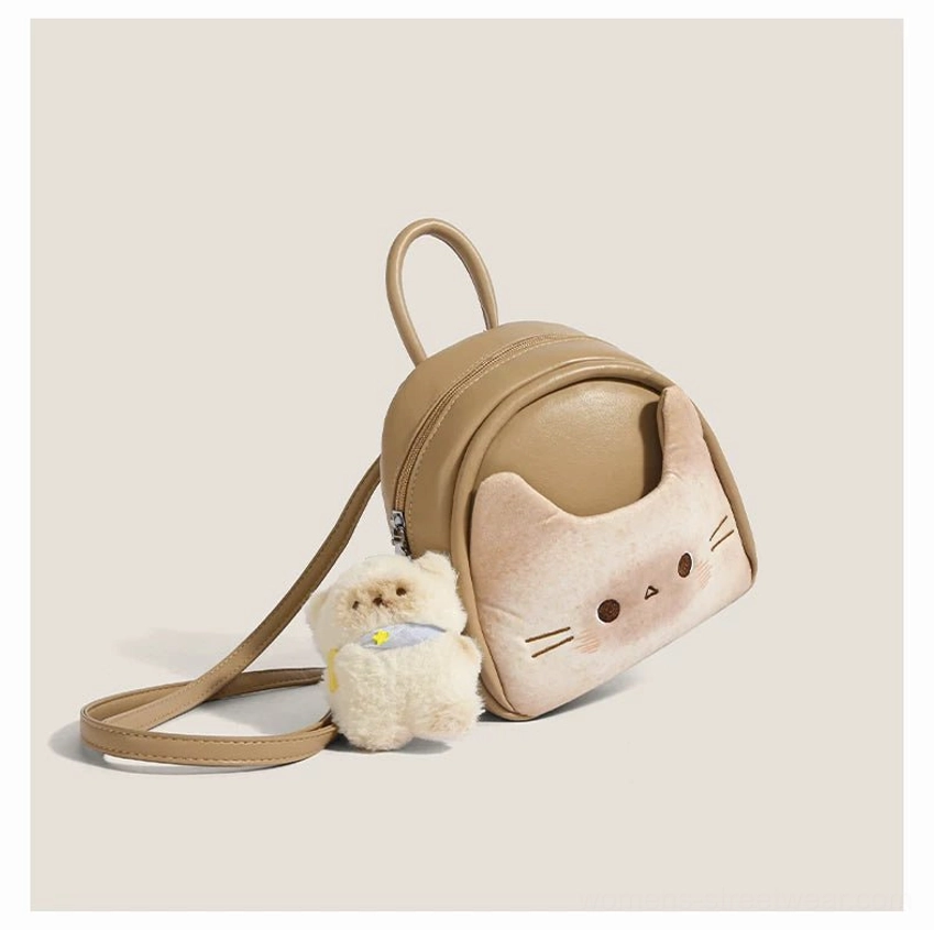 Left side three quarter view of a toast beige mini cat backpack showing the rounded profile, soft faux leather texture, adjustable strap hardware, and plush puppy charm