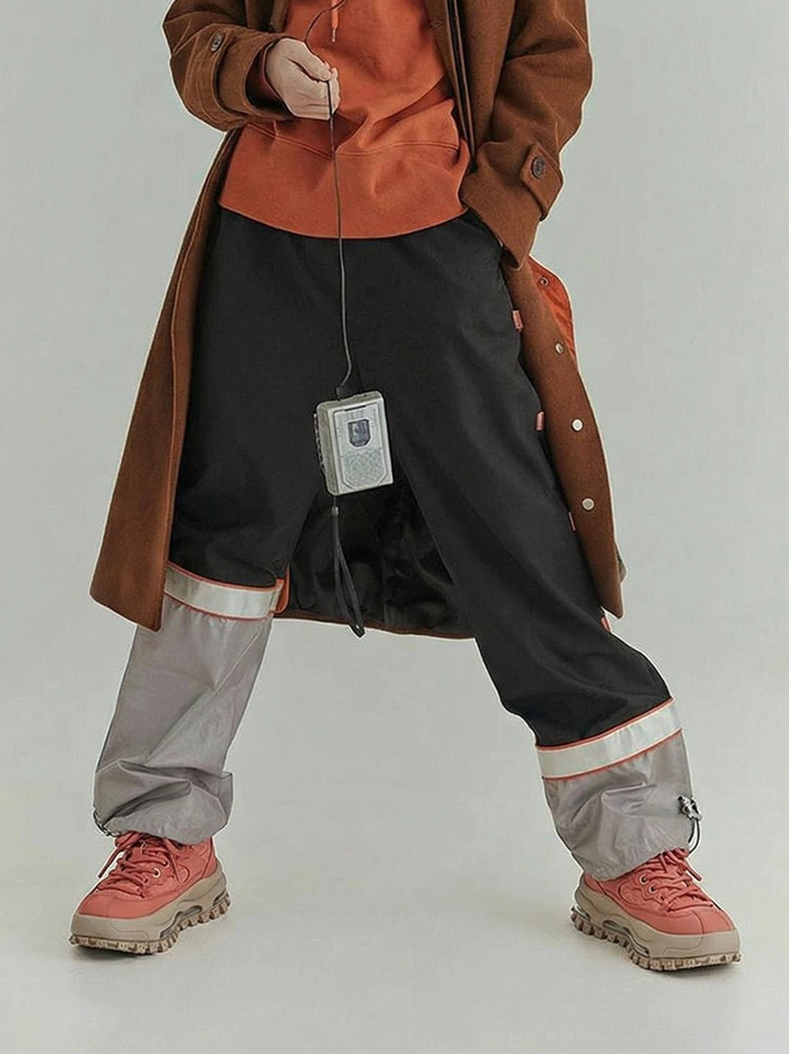 Terracotta platform trail sneakers styled with long coat and contrast panel pants for urban streetwear look