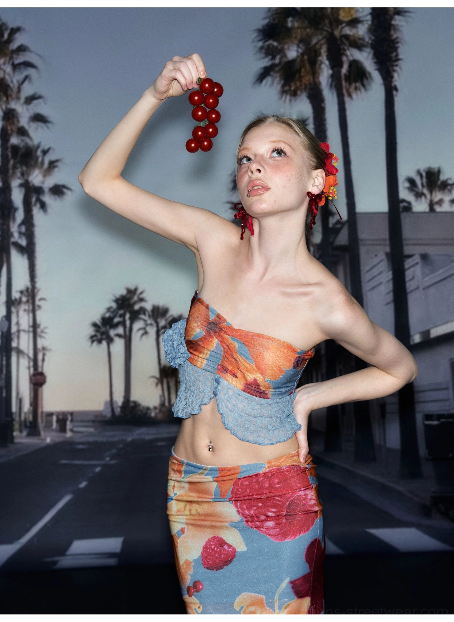 Front view of a model wearing a tropical fruit print strapless lace trim crop top with a coordinated skirt