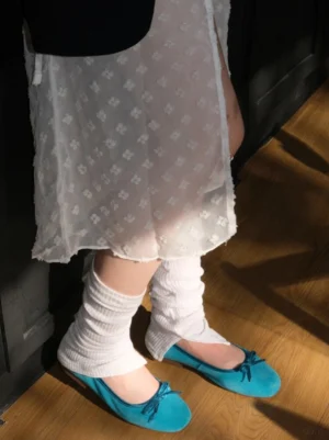 Turquoise bow ballet flats styled with white ruffled leg warmers and sheer embroidered skirt indoors