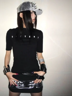 Front view of a black slim-fit Sakyant graphic tee with half-high neckline, white chest lettering, and elbow-length sleeves styled with punk accessories