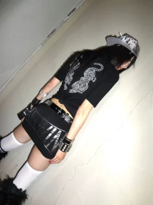 Back three-quarter view of a black twin tiger graphic tee showing mirrored tattoo-inspired tiger artwork styled with white thigh-high socks