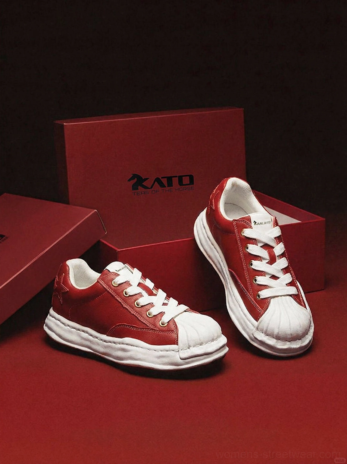 Two pairs of red molded-toe sneakers displayed on burgundy fabric with white midsoles and black outsole trim