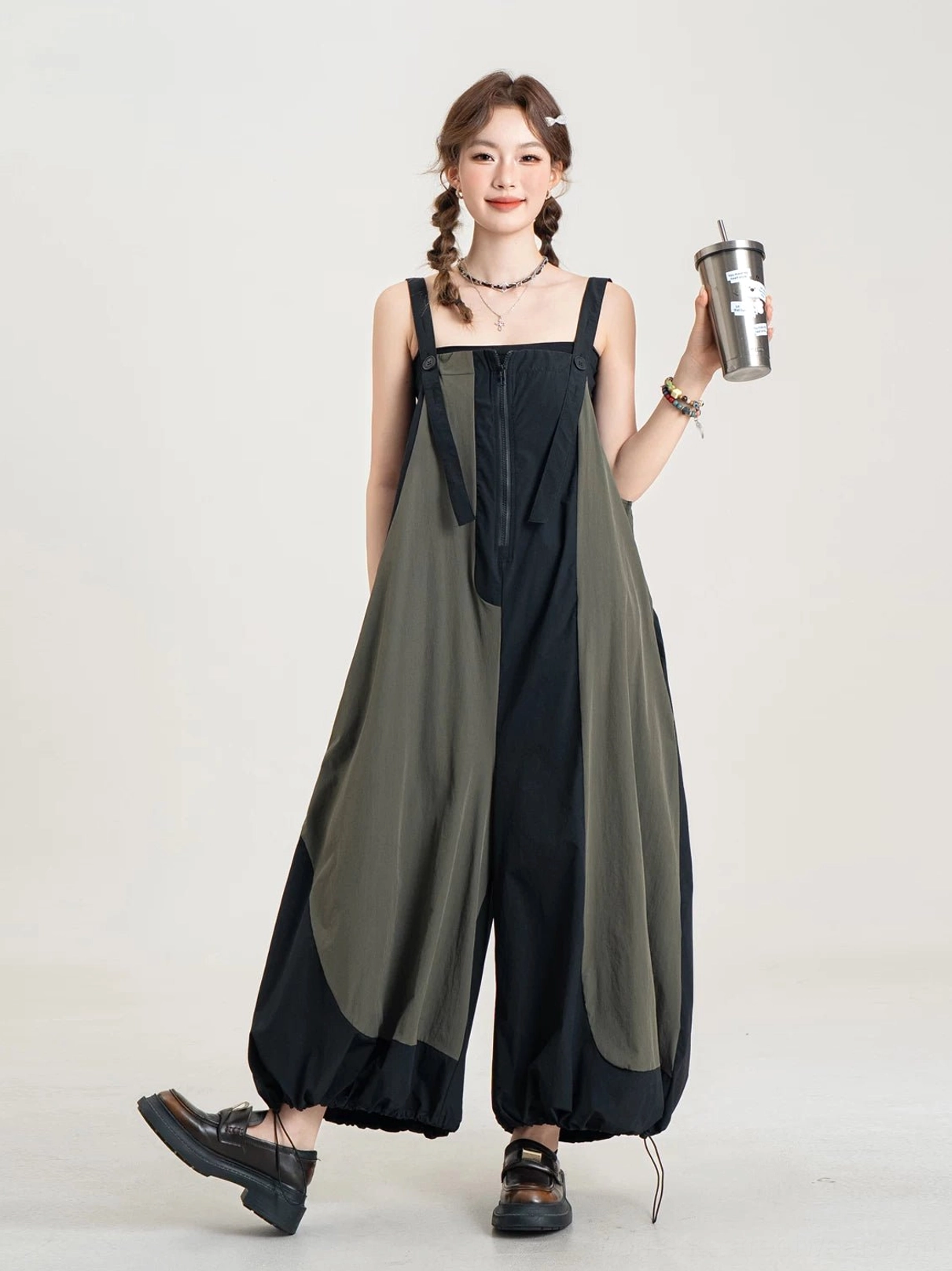 Full-body view of a two-tone black and army olive jumpsuit with wide balloon legs, adjustable suspenders, and gathered drawstring hems