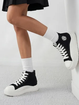 Female model wearing two-tone canvas platform high-top sneakers with white crew socks and black pleated skirt low angle product shot