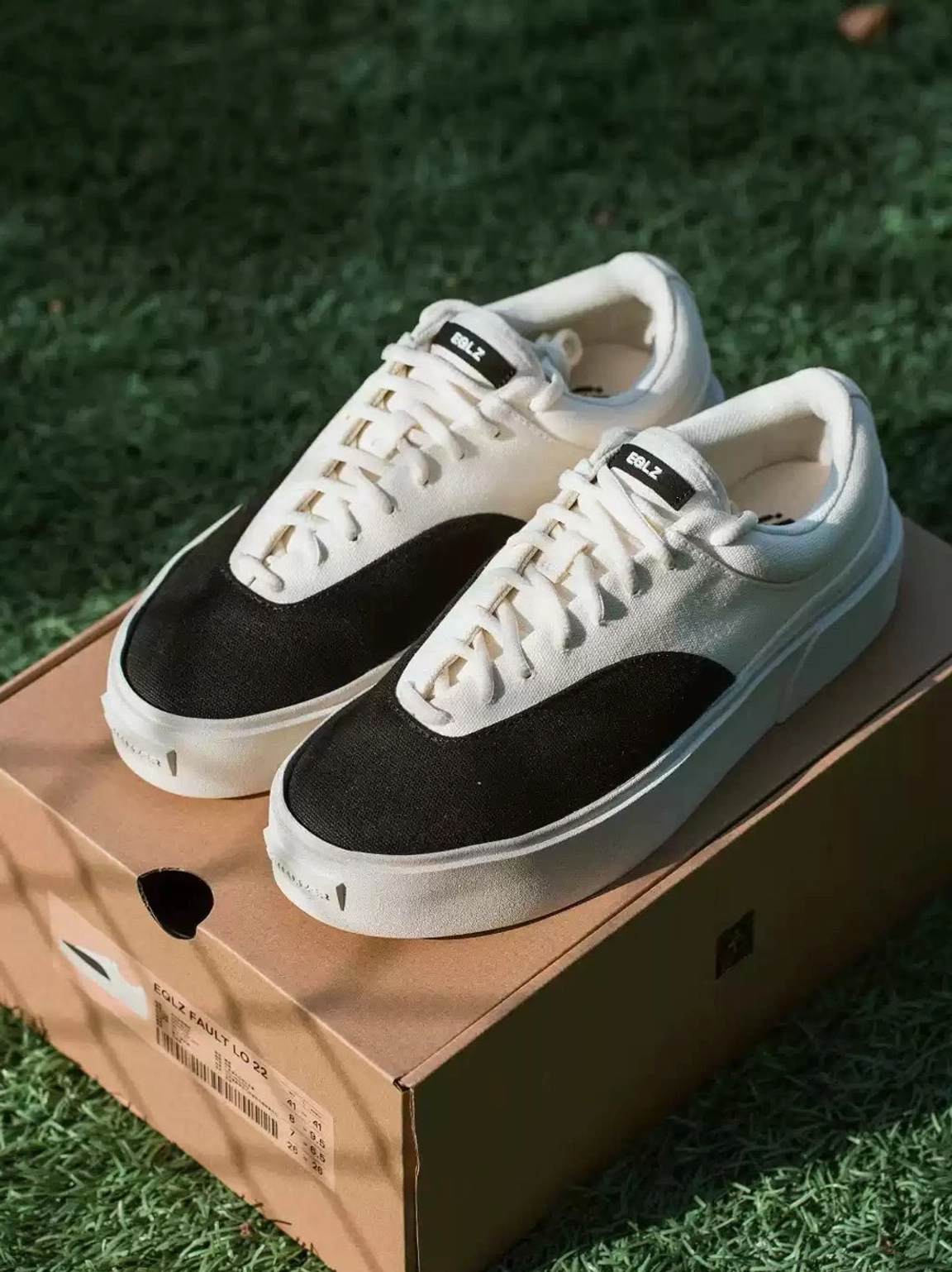 Pair of black and egret white two-tone canvas platform skate shoes shown on a shipping box with thick rubber outsole