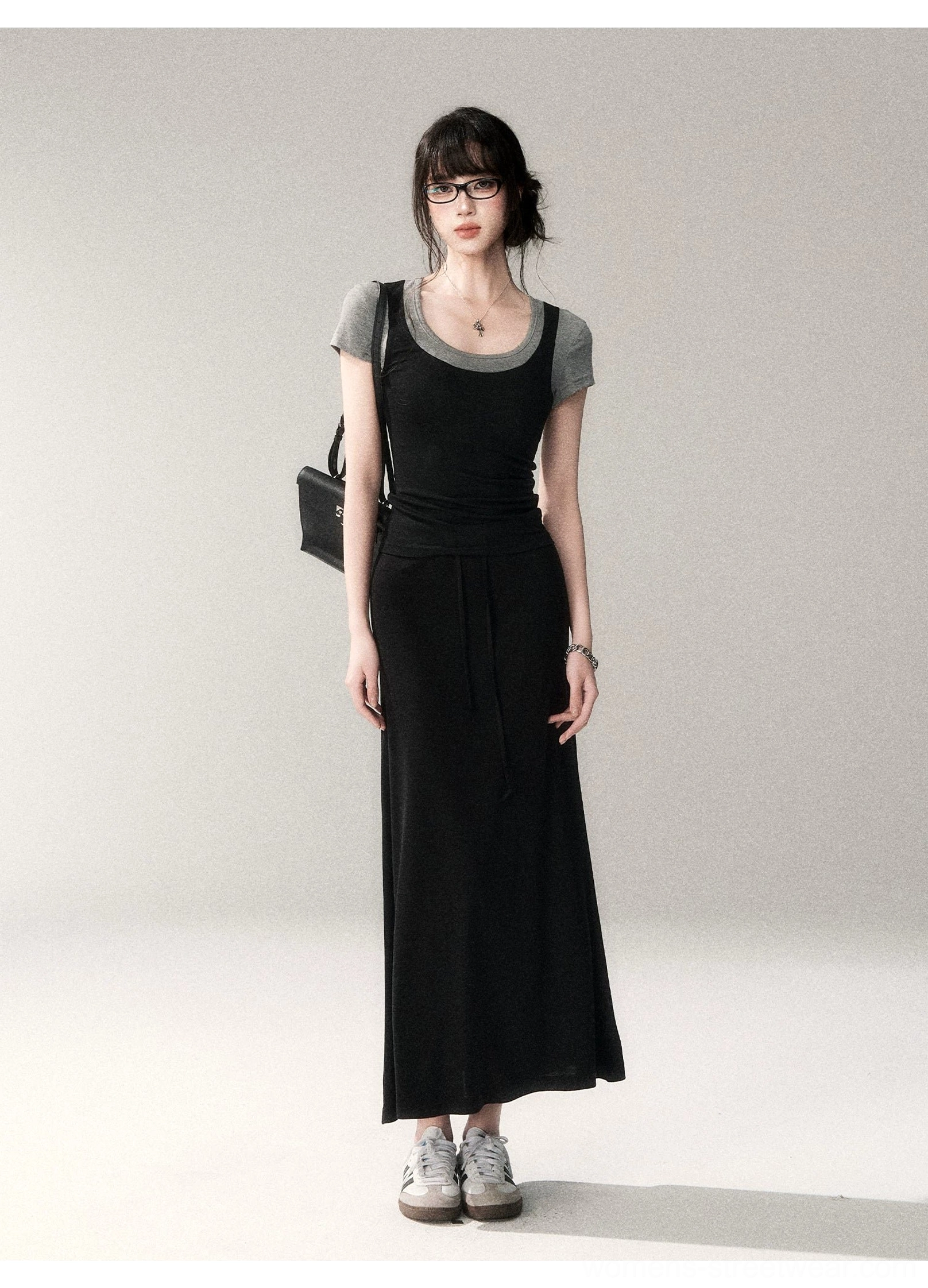 Full front view of a slim two-tone layered scoop neck top worn under a relaxed black maxi dress with gray casual sneakers