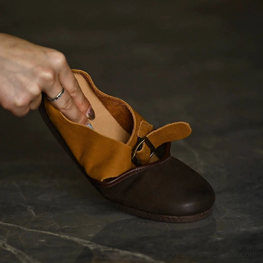 Handheld close-up of two-tone leather Mary Jane flat with dark brown upper tan strap and metal buckle