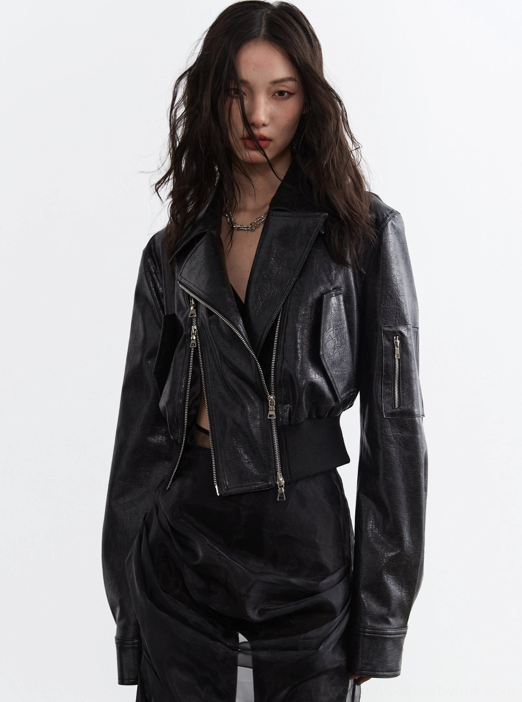 Front view of a women's ultra-cropped black faux leather biker jacket with asymmetrical silver zipper, notched lapels, relaxed sleeves, ribbed hem, and sleek streetwear styling