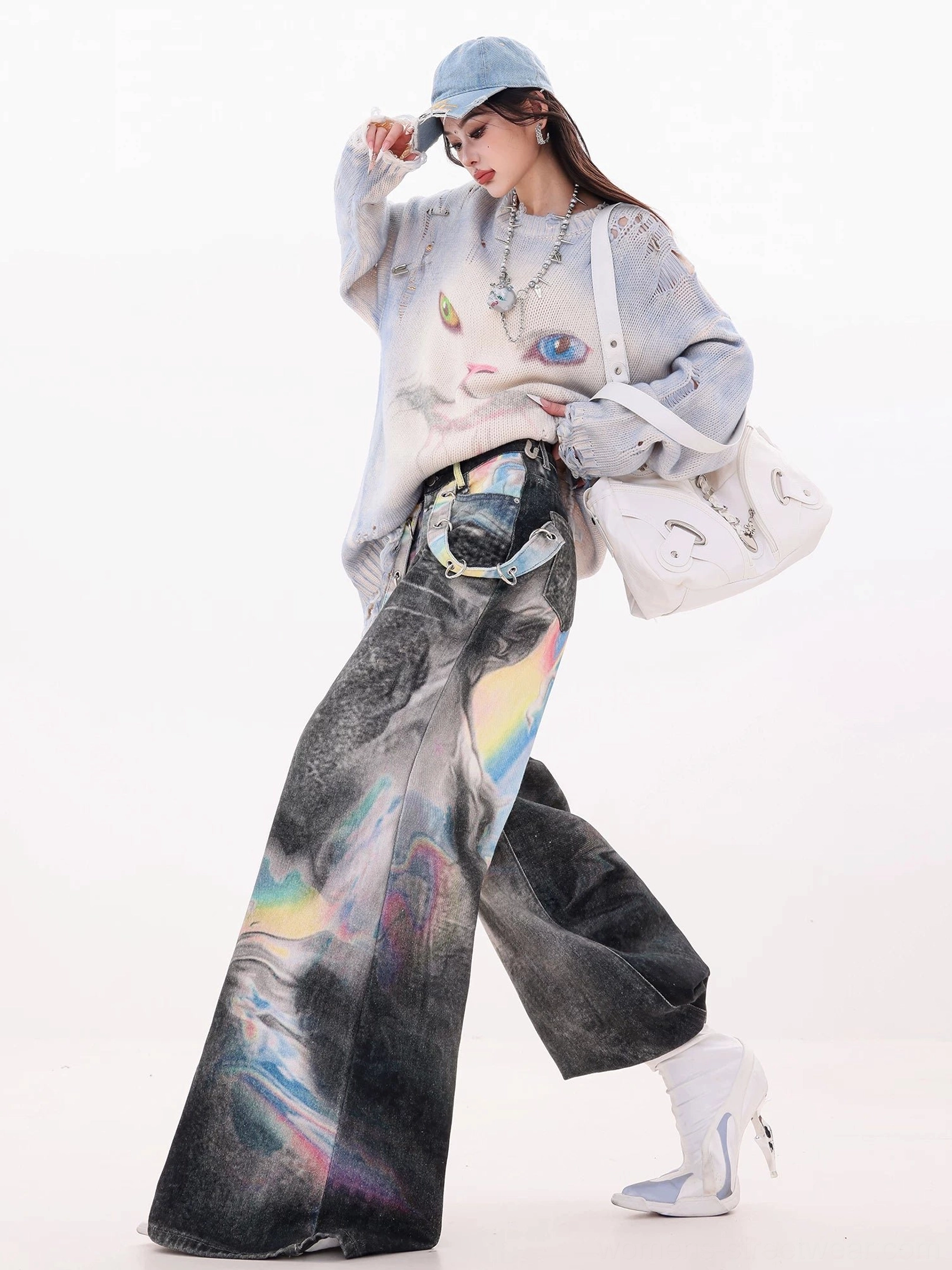Low-angle side view of ultra wide-leg holographic gradient denim jeans styled with a cropped knit sweater, white shoulder bag, and white heeled boots
