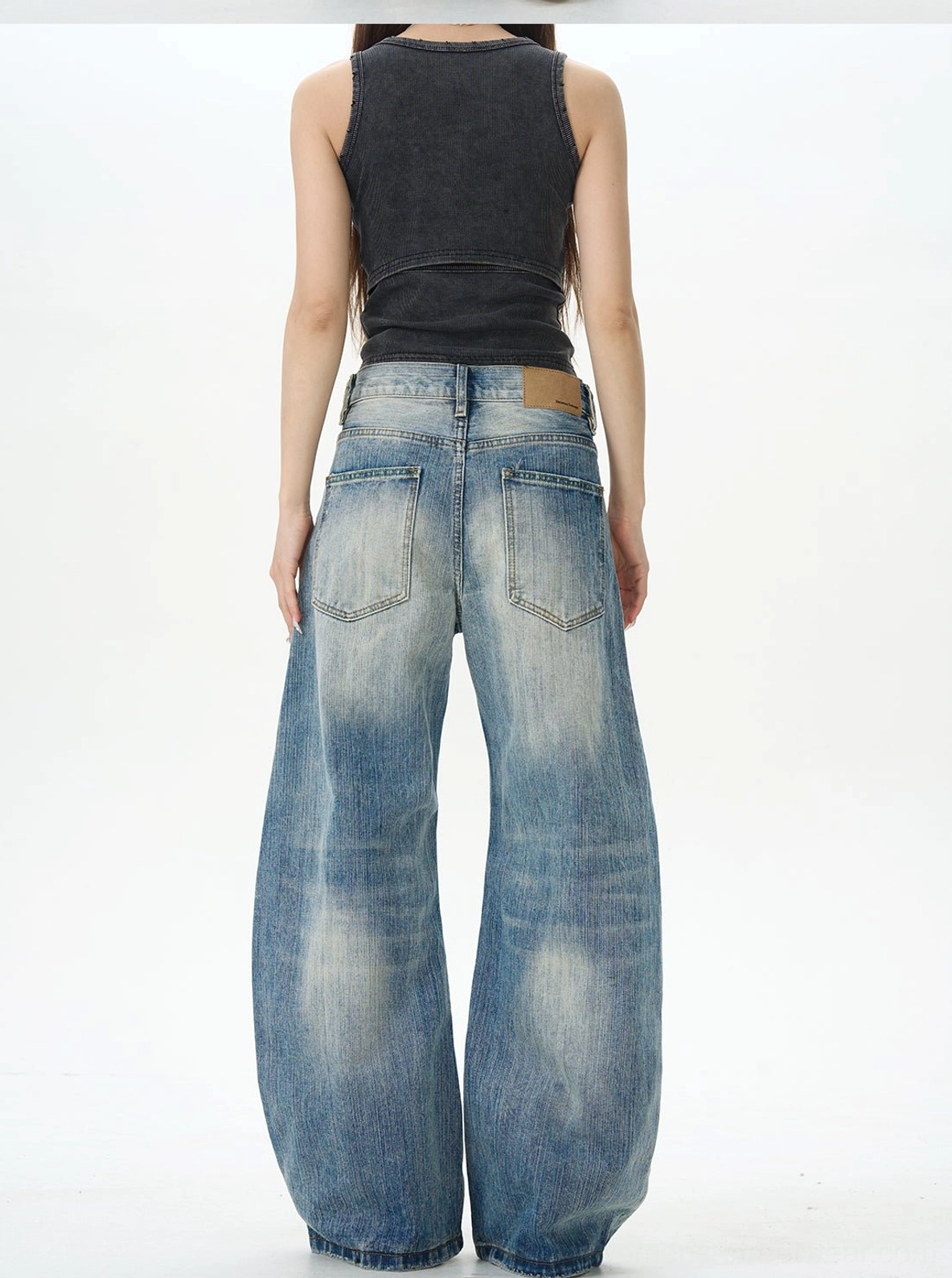 Back view of unisex retro wide-leg jeans with branded-style leather waist patch, two rear pockets, loose silhouette, and black tank top styling