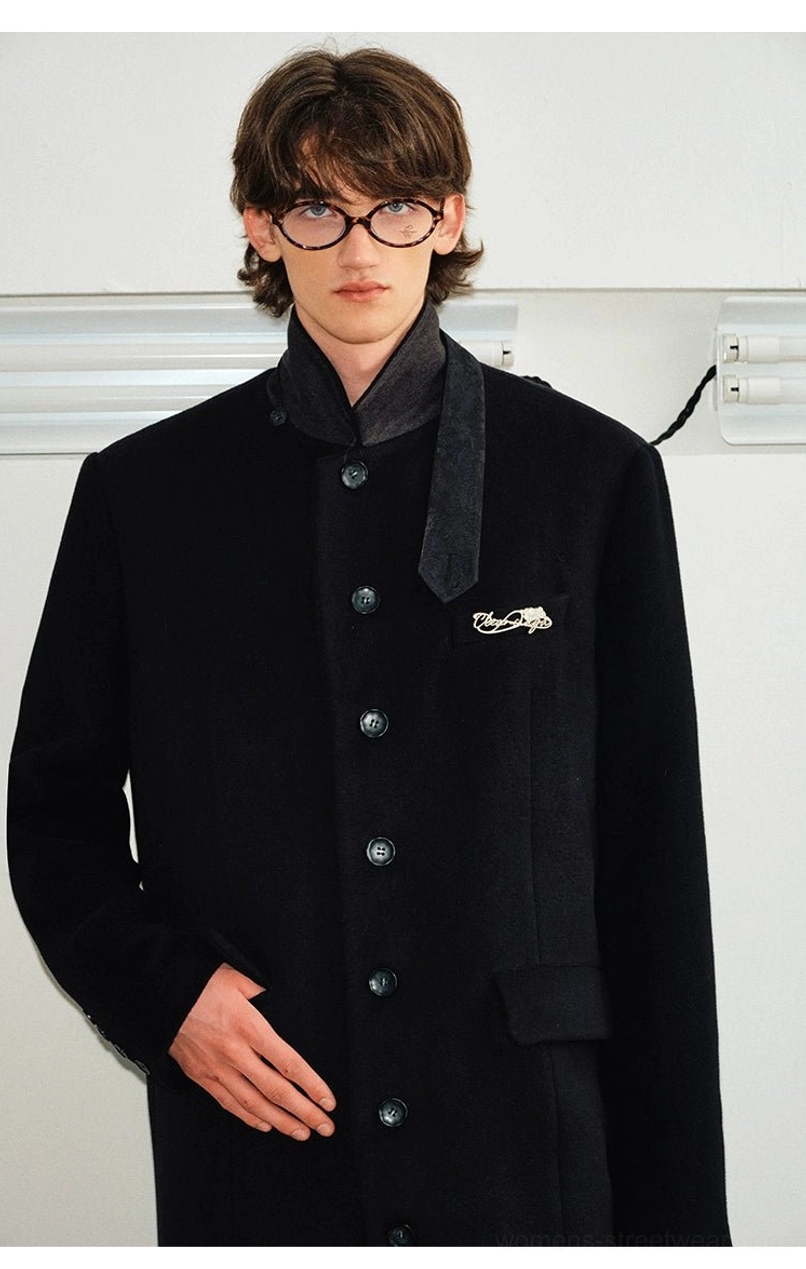Black wool blend overcoat close-up featuring contrast velvet trimmed stand collar round buttons and textured fabric